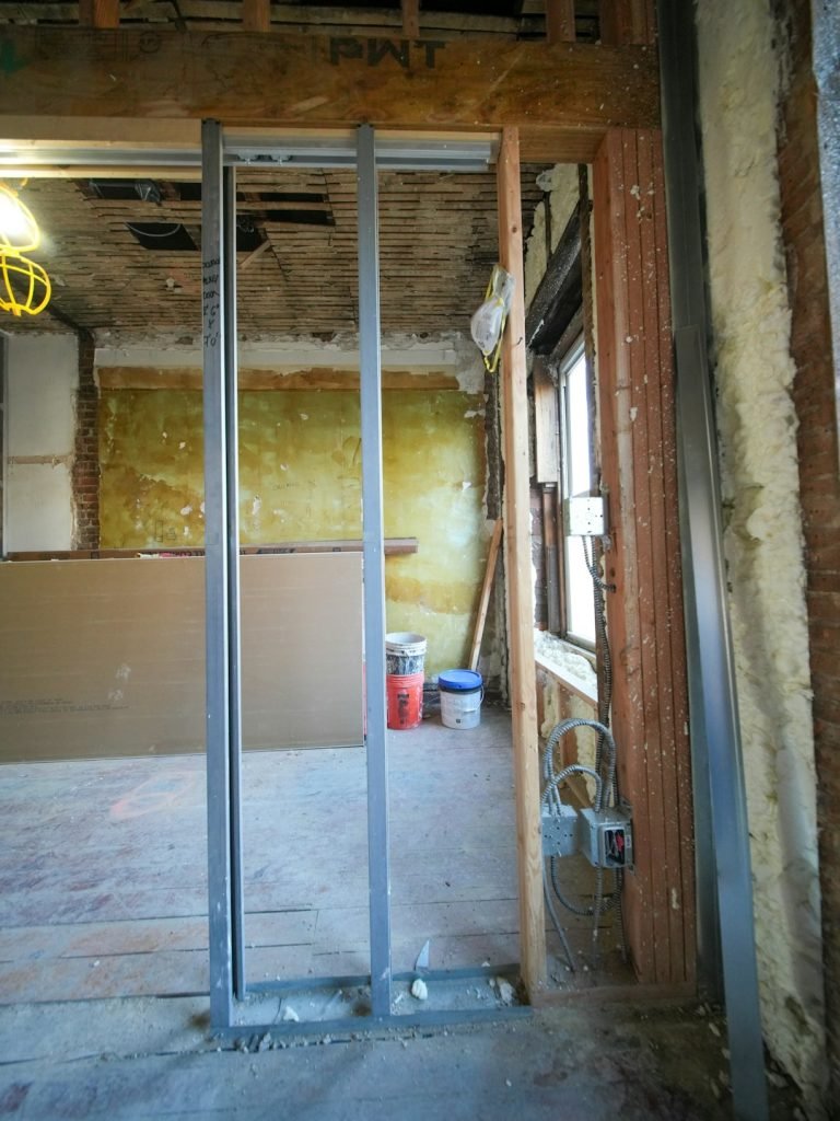A three-story brownstone stands in mid-transformation, captured at the raw and honest “before” stage of a full interior renovation. These images document a moment that usually disappears once the walls are closed and the finishes are installed — exposed framing, stripped ceilings, rough staircases, and open corridors that reveal the building’s original structure and hidden history. Light spills in through skylights and tall windows, cutting through layers of dust and unfinished surfaces, creating a quiet contrast between decay and renewal. The space feels both industrial and intimate: narrow